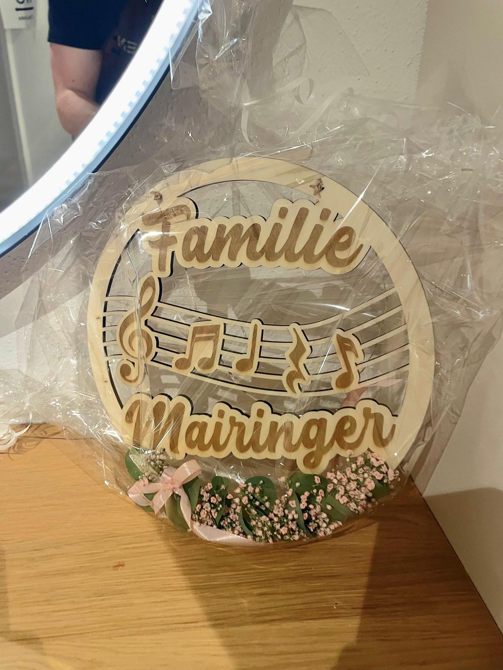 Personalisierter Holzloop mit dem Schriftzug „Familie Mairinger“, Notenlinien und Musiknoten, dekoriert mit Schleierkraut und Röschen